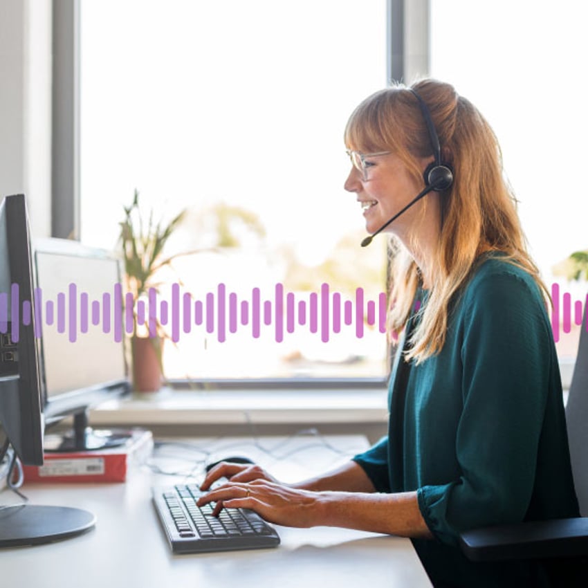 Photo of a smiling woman working in an office. She is talking to a customer on her headset while typing notes into her computer. In the background, a series of small purple vertical lines runs across the frame.